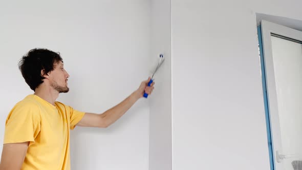 A Man Wearing a Yellow Tshirt Paints the Wall Using a Roller Painter alt