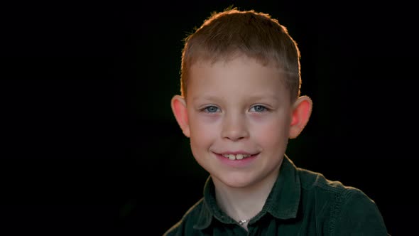 portrait of boy smiling and looking at camera on dark studio background