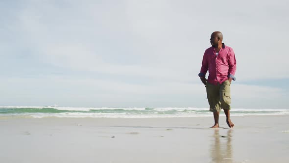 African american senior man walking on a beach looking at the sea alt