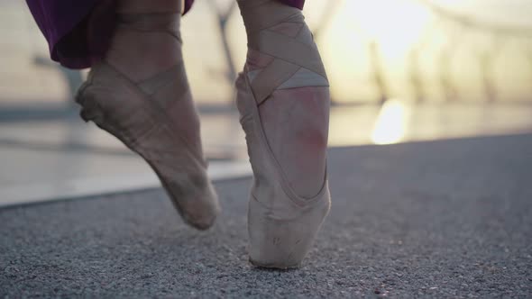 Close-up of Female Feet in Pointe Shoes Walking on Asphalt Bridge on Sunrise or Sunset alt