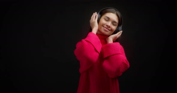 Beautiful Woman in a Bright Pink Sweater Enjoys Music in Wireless Headphones