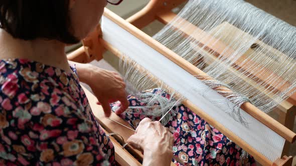 Woman with heddle hook in her hand is warping a weaving handloom. Threading the table loom