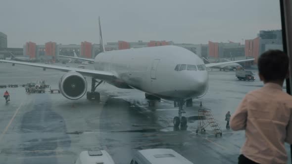 Kid in the airport looking at plane through the terminal window alt