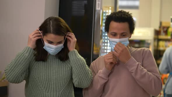 Multiethnic Couple Putting on Masks in Supermarket alt