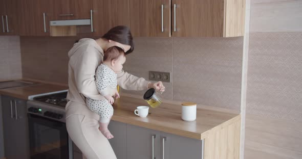 A Mother With A Small Child In Her Arms Makes Tea