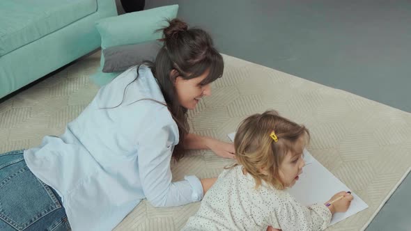 Mom and Daughter Lying on Carpet on the Floor Drawing on Paper Together alt