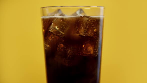 Glass Full of Cola Fizzy Drink with Ice Cubes. Cold Sparkling Soda on Yellow Background alt