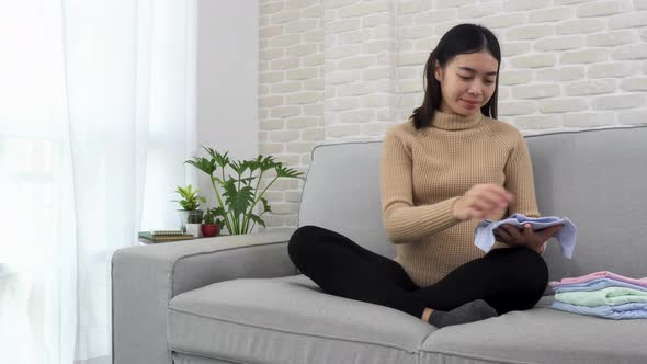 Young pregnant asian woman sitting cross legged on a gray sofa