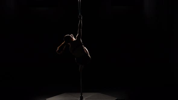 Dancer Spinning on a Pole in a Dark Studio . Black Background. Silhouette alt