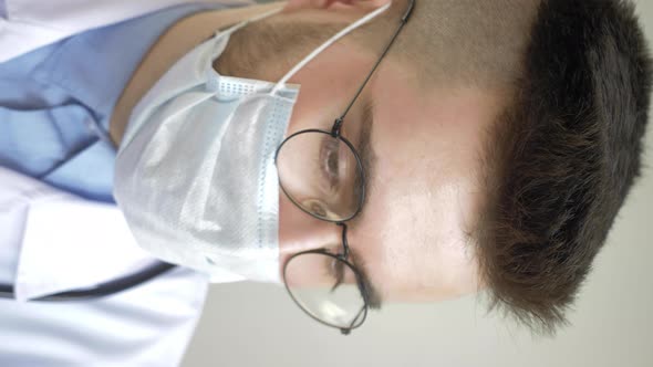 Young Male Doctor in Glasses and Mask Sitting at Home with a Patient in a Bright Room at Home alt
