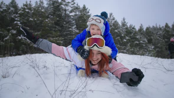 Active Winter Holidays Happy Mother and Son with a Phone in Their Hands Quickly Go Down Snowy Slope