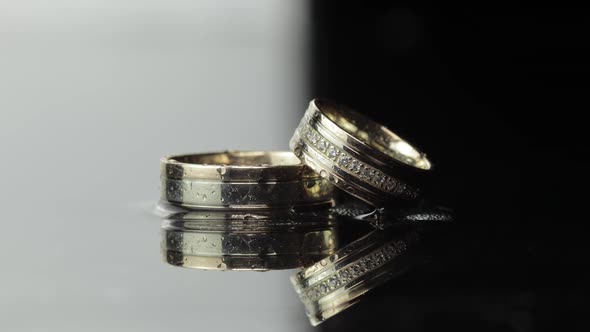 Wedding Rings on Black and White Water Surface Shining with Light. Close Up alt