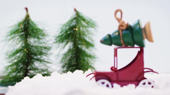 Toy car carrying christmas tree on fake snow alt