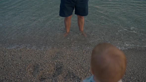 Toddler Walks on Pebbles to Father Standing in Sea Water alt