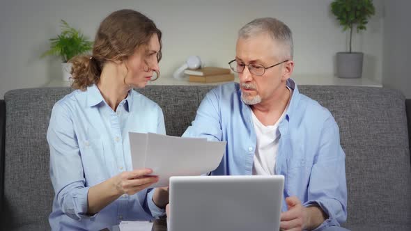 An Agitated Elderly Couple Checks the Bills on Their Laptop and Discusses Debts