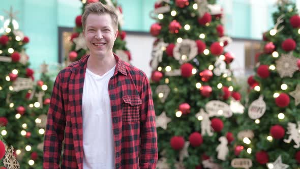 Happy Young Man Smiling Against Illuminated Christmas Trees Outdoors alt
