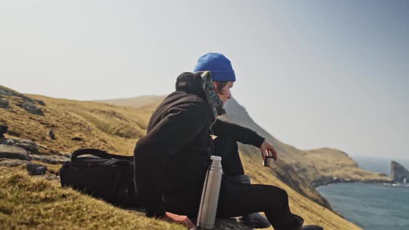 Man Traveling Alone Sitting By the Hill with a Hot Drink and an Overlooking alt