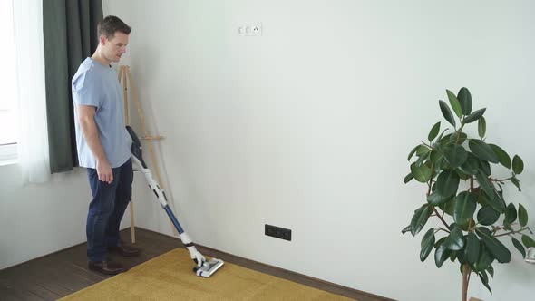 Handsome Caucasian Man Cleaning Floor Carpet with Vacuum Cleaner in Modern White Living Room