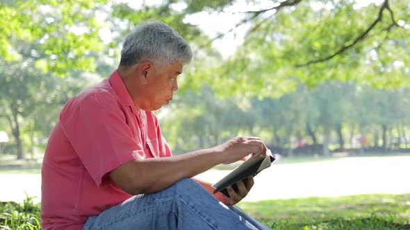 Asian elderly man Sitting in the park reading a book in the morning.