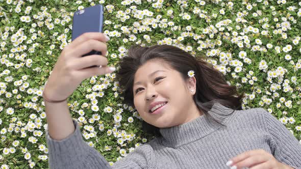 Happy asian girl taking a selfie with a daisy between her hair and daisies co alt