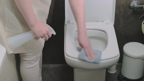 A woman cleans up the bathroom by wiping the toilet bowl with a rag