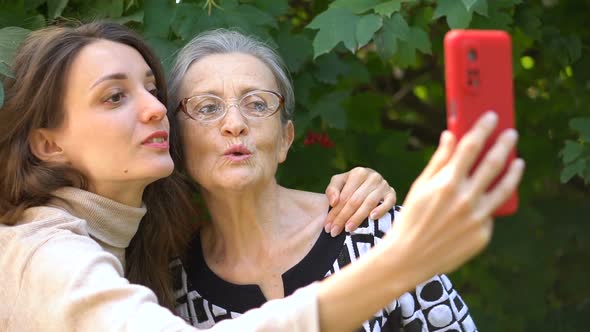 Adult Daughter and Senior Mum are Taking Selfportrait Picture Selfie on Red Smartphone Together alt