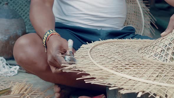Man cutting surplus of bamboo reed on a handcrafted hat with scissors. Process of making handcrafted alt