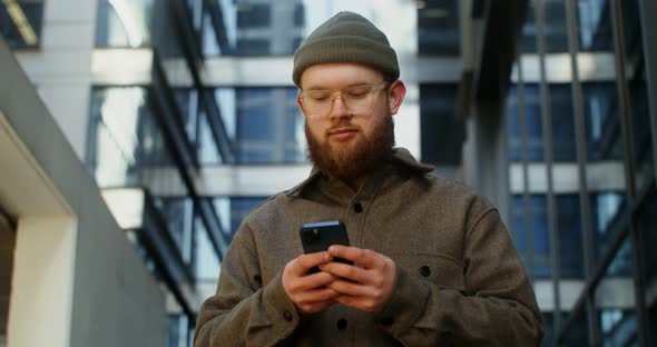 A Young Man is Typing on a Mobile Phone While Walking Around the Business Center alt
