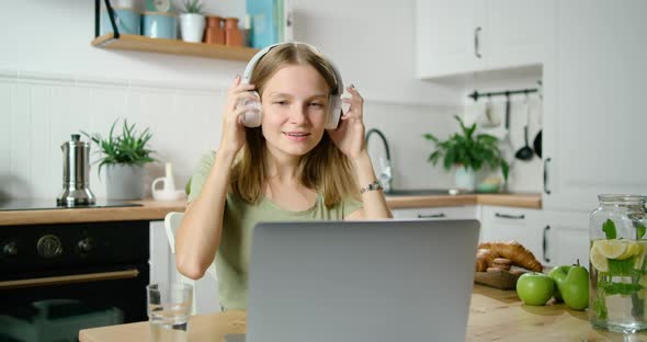 Woman Puts on Headphones and Talks Online By Video Call Using Laptop in Kitchen