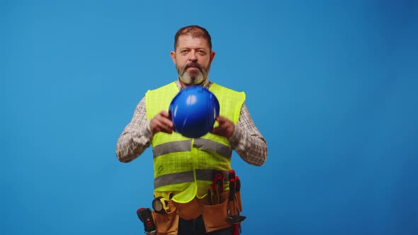 Smiling Senior Man Builder in Vest and Hardhat Against Blue Background