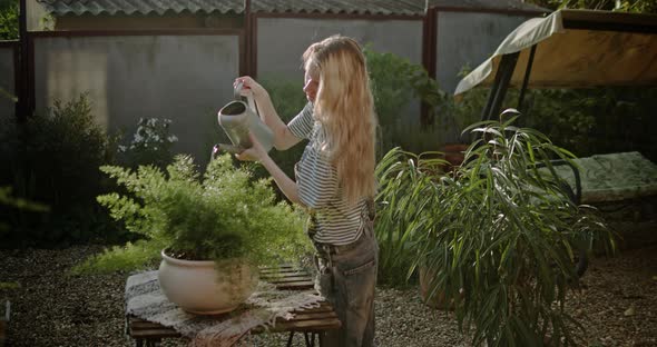 Young Girl with a Watering Can Watering Flowers in a Summer Garden