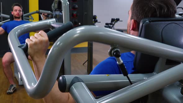 A Young Fit Man Trains on a Machine in a Gym - Closeup From Behind alt