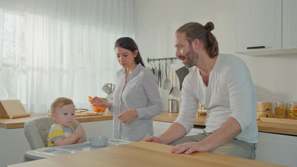 Caucasian attractive parents feeding healthy foods to baby toddler in kitchen room at house. alt