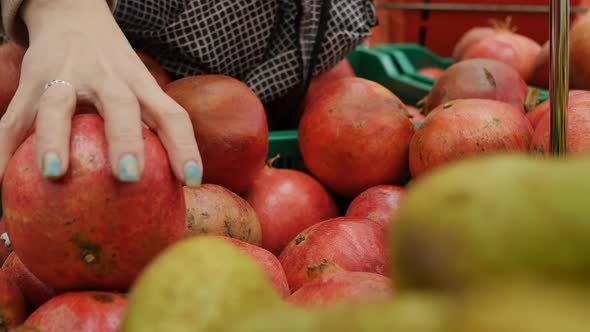 the Hand of a Caucasian Woman Selects a Large Red Pomegranate in the Market