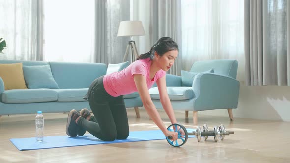 Asian Woman In Sportswear Is Working Out With Exercise Wheel At Home In The Living Room alt