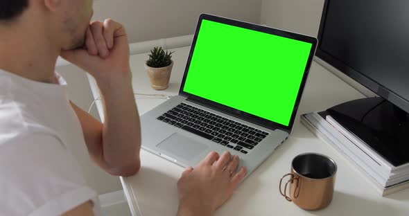 Over the shoulder shot of European millennial hipster man typing and looking at laptop green screen alt