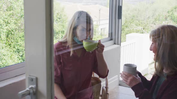 Mother and daughter talking to each other while drinking coffee at home alt