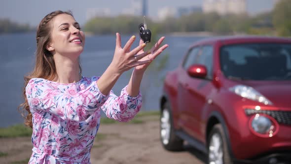 A Pretty Girl is Standing in Front of the Car Throwing Up Keys Catching and Waving Them in the Frame alt