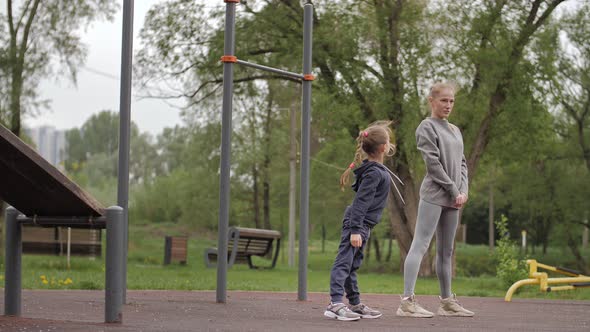  Mother and Daughter Doing Exercises on Open Air Sport Playground alt