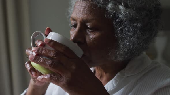 Close up of senior african american woman drinking coffee while sitting on the bed at home alt