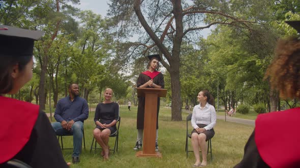 Joyful Male Arab Graduate Giving Talk to Fellow Students at Graduation Day alt