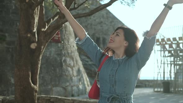 Young smiling brunette woman with red lipstick in denim overalls  sits on sunlights and enjoy her alt