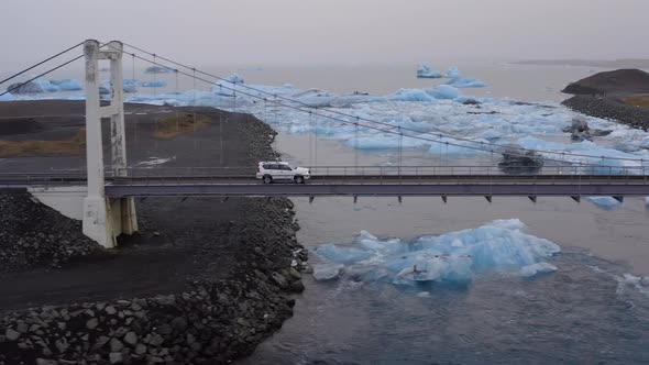 Car Driving on a Cable Bridge Above the Glacial River with Large Ice Splinters alt