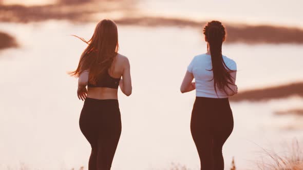 Two Young Women Jogging on Wheat Field While Sunset alt