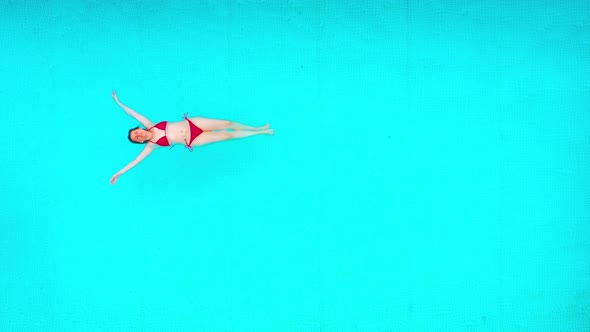 View From the Top As a Woman in a Red Swimsuit Lying on Her Back in the Pool alt
