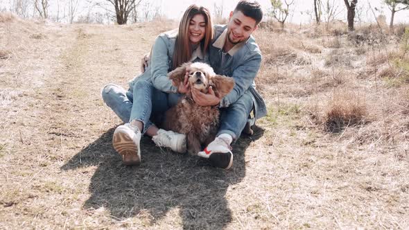 Pretty Young Woman and Man Are Sitting in the Field Walking with a Cute Dog alt