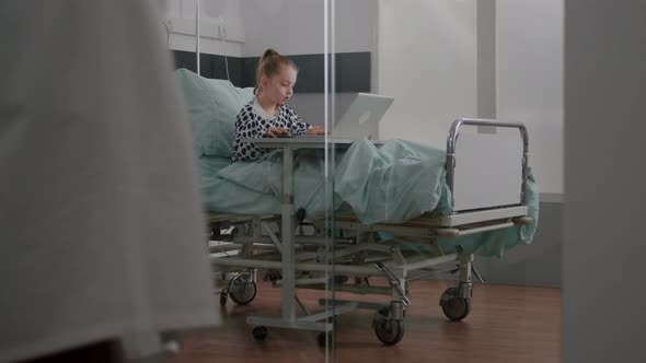 Sick Child Relaxing in Bed Playing Cartoon Video Games on Laptop Computer During Medical Examination alt