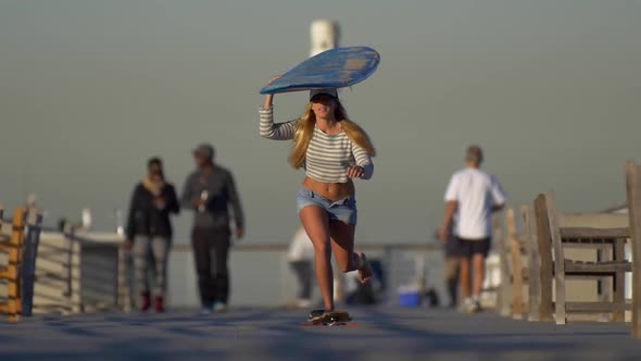 A young woman longboard skateboarding while balancing a surfboard on her head. alt
