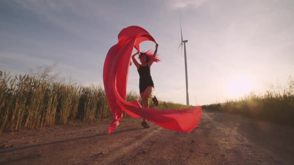 Woman with Pieces of Red Cloth Run to the Wind Generator in the Field alt