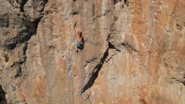 Aerial View From Drone of Strong Muscular Young Man Climbs on Big Rocky Wall By Challenging Rock alt
